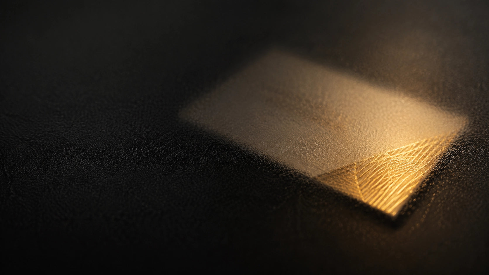 Business card under frosted glass with gold foil catching light.